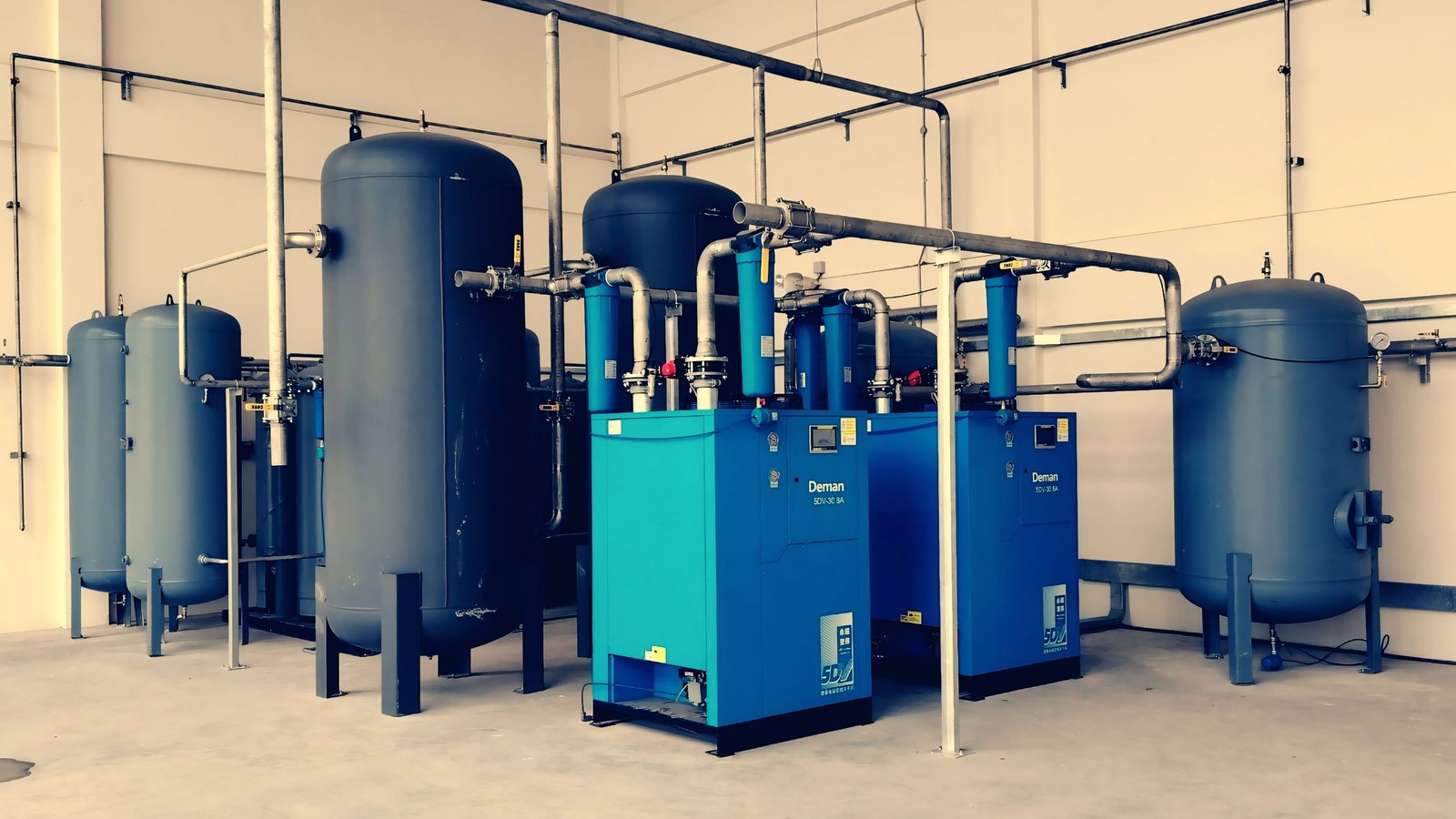 A vertical air receiver stood next to a rotary screw compressor in a plant room